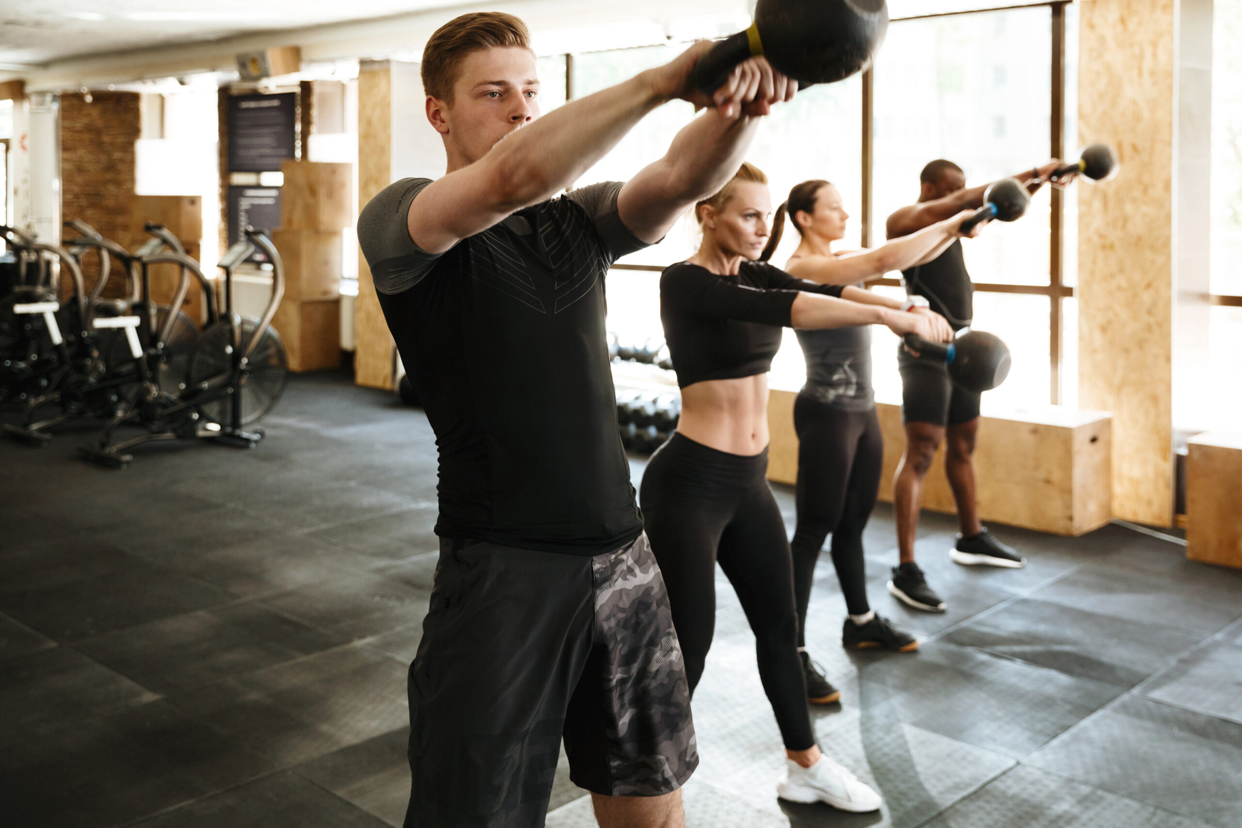 A diverse group of members performing kettlebell swings in a structured, coach-led HIIT training session.